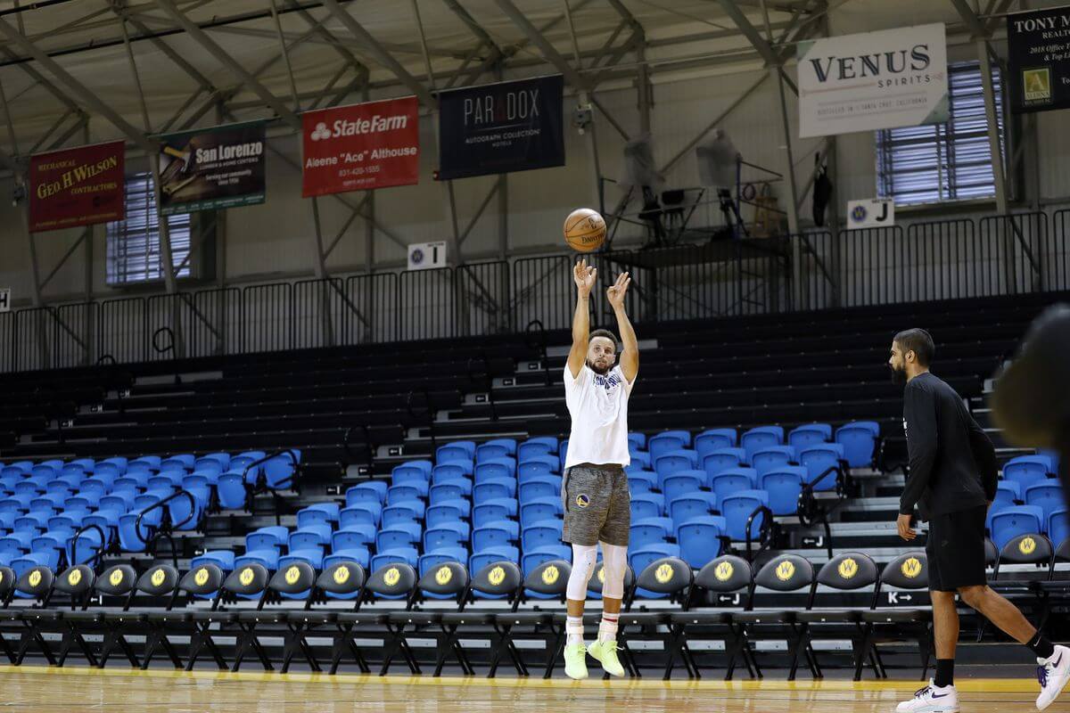 Steph Curry tengah berlatih, melempar bola basket dari pinggir arena kosong